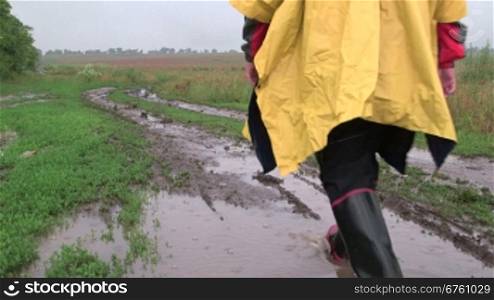 Man wearing yellow raincoat goes on a dirt country road through the field in rain