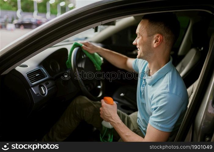 Man wipes car interior with a rag, hand auto wash station. Car-wash industry or business. Male person cleans his vehicle from dirt outdoors. Man wipes car interior with a rag, hand auto wash