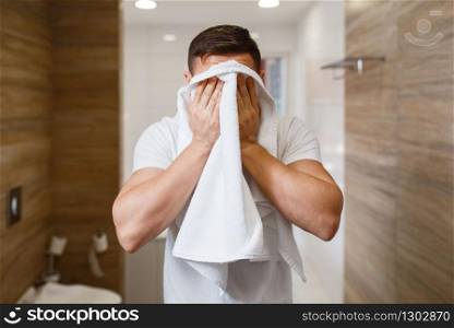 Man wipes his face with a towel, front view, routine morning hygiene. Male person at the sink performs skin and body treatment procedures. Man wipes his face with a towel, morning hygiene