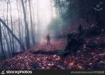 Man with a lamp at the dark foggy forest