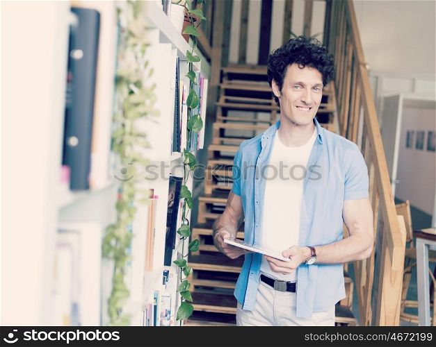 Man with a magazine standing next to bookcase