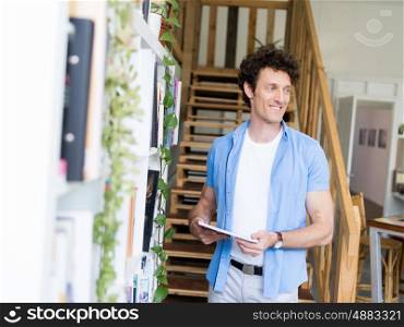 Man with a magazine standing next to bookcase
