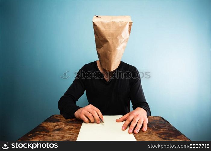 Man with a paper bag over his head is writing a letter