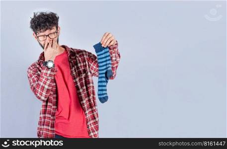 Man with a smelly sock in his hand holding his nose. Person with a stinky sock in his hand, concept of smelly socks and uncleanliness