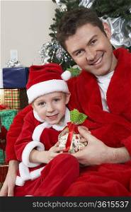 Man with arm around boy (5-6) in Santa hat holding Christmas present