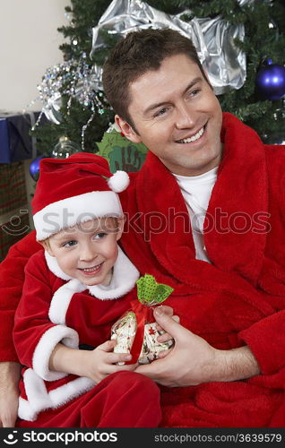 Man with arm around boy (5-6) in Santa hat holding Christmas present