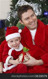 Man with arm around boy (5-6) in Santa hat holding Christmas present