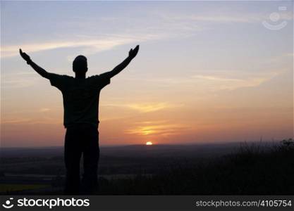 man with arms outstretched in front of sunset