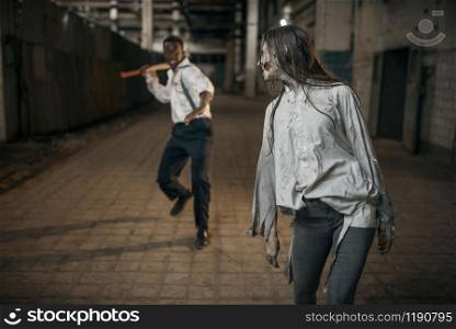 Man with axe attacked female zombie in abandoned factory, scary place. Horror in city, creepy crawlies, doomsday apocalypse, bloody evil monsters