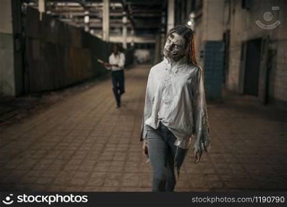 Man with axe catching up female zombie in abandoned factory, scary place. Horror in city, creepy crawlies, doomsday apocalypse, bloody evil monsters