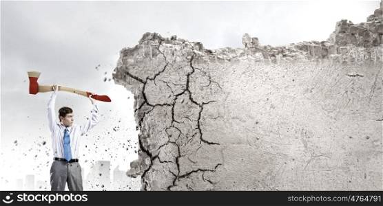 Man with axe. Young determined businessman crashing wall with axe