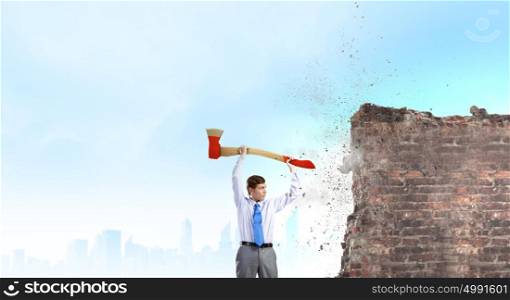Man with axe. Young determined businessman crashing wall with axe