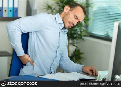 man with back pain in armchair at office