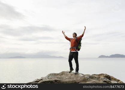 Man with backpack and arms raised  enjoying the beautiful morning view of the coast