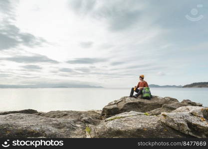 Man with backpack and sitting on the rocks while enjoying the beautiful morning on the beach