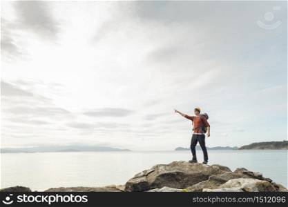 Man with backpack enjoying and pointing to the beautiful morning view of the coast
