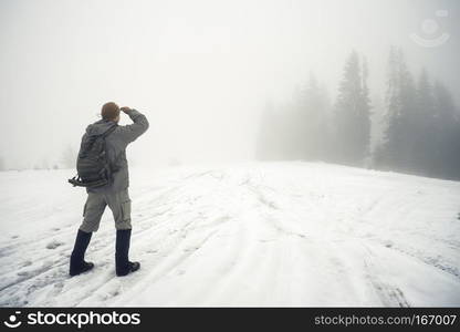 Man with backpack in the winter mountains peers into the foggy distance. Winter landscape. The concept of freedom, travel and choice of ways.. Man with backpack in the winter mountains peers into the foggy d