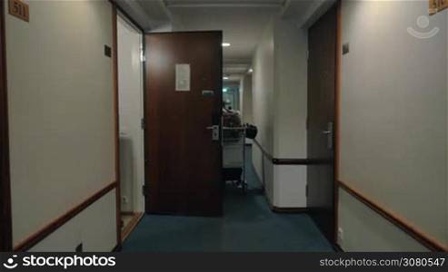 Man with backpack leaving hotel room and walking in the hallway rolling cart with luggage