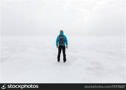 Man with backpack standing alone on the lake ice and staring forward. Cold cloudy winter day.. Man with backpack standing alone on the lake ice and staring forward. Cold cloudy winter day