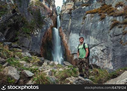 Man with backpack standing in front of waterfall. Traveling to the waterfall