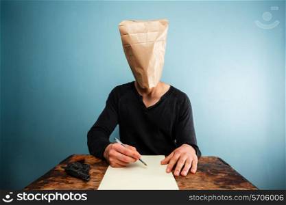 Man with bag over his head writing a note at desk with gun