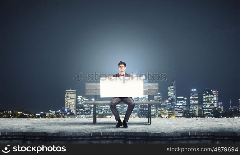 Man with banner. Young man in glasses sitting on bench with white banner