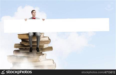 Man with banner. Young man with white blank banner sitting on pile of books