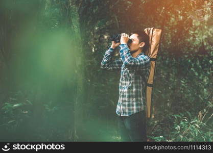 Man with binoculars telescope in forest looking destination as lost people or foreseeable future. People lifestyles and leisure activity concept. Nature and backpacker traveling jungle background