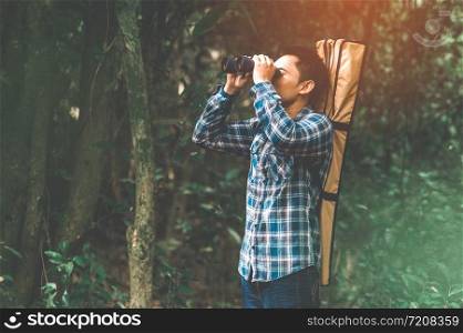 Man with binoculars telescope in forest looking destination as lost people or foreseeable future. People lifestyles and leisure activity concept. Nature and backpacker traveling jungle background