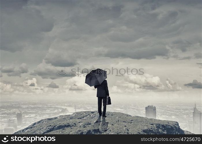 Man with black umbrella. Back view of businessman with umbrella and suitcase standing on mountain top