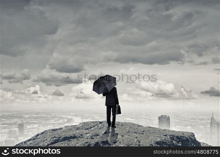 Man with black umbrella. Back view of businessman with umbrella and suitcase standing on mountain top