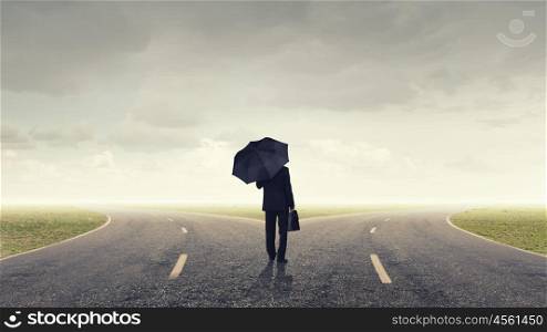 Man with black umbrella. Back view of businessman with umbrella and suitcase walking on road