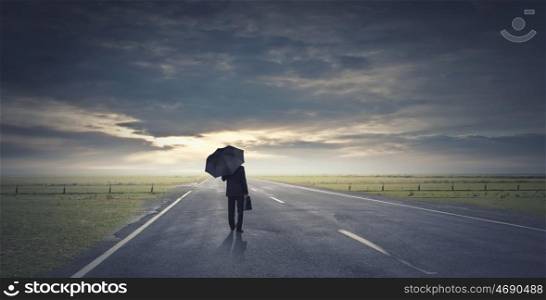 Man with black umbrella. Back view of businessman with umbrella and suitcase walking on road