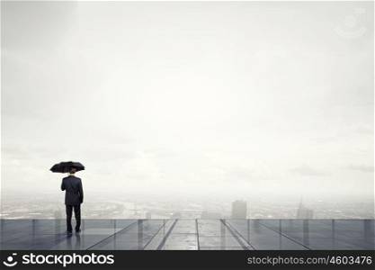 Man with black umbrella. Back view of businessman with umbrella looking at city