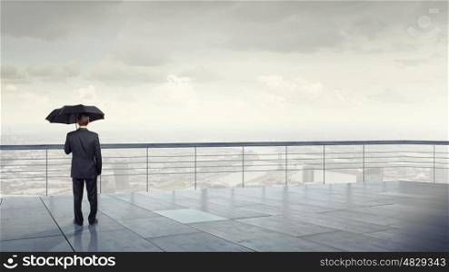 Man with black umbrella. Back view of businessman with umbrella looking at city