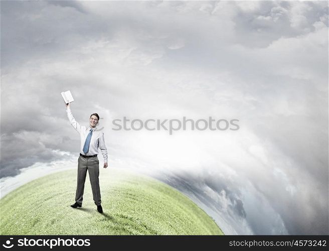 Man with book in hand. Young screaming businessman on hill reaching hand with opened book