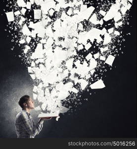 Man with book on dark background. Young man with opened book in hands and pages flying in air