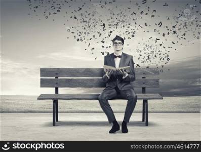 Man with book. Young man in suit sitting on bench with book in hands