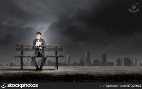 Man with book. Young man in suit sitting on bench with book in hands