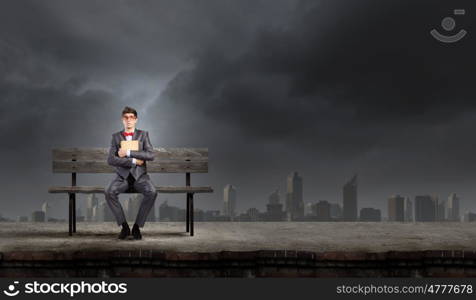 Man with book. Young man in suit sitting on bench with book in hands