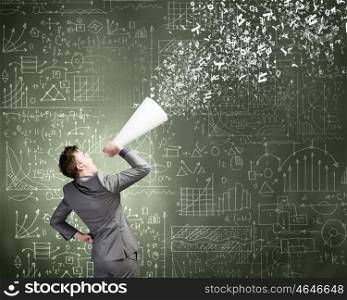 Man with bullhorn. Young businessman speaking in trumpet with business sketches on wall