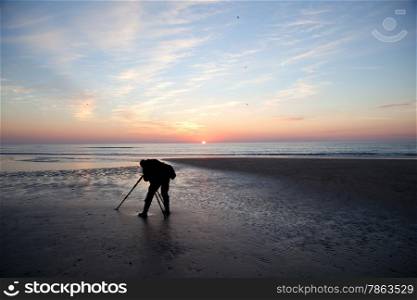 man with camera on tripod alone on beach at sundown on the North Sea cost of the netherlands