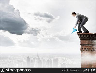 Man with can. Young businessman standing on cloud and watering something below