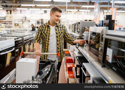 Man with cart choosing microwave in electronics store. Male person buying home electrical appliances in market. Man choosing microwave in electronics store