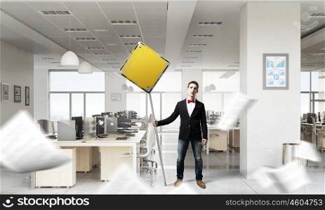 Man with caution signboard. Young businessman with caution yellow sign in office interior