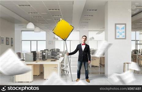 Man with caution signboard. Young businessman with caution yellow sign in office interior