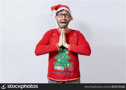 Man with christmas hat with hands together in pleading gesture. Christmas guy with hands together begging for a Christmas wish, Person in christmas hat with desperate pleading gesture