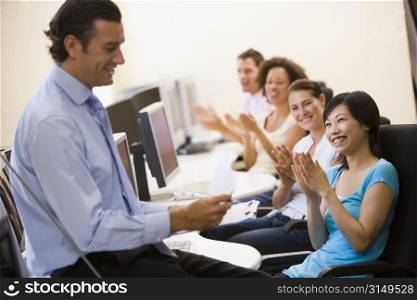 Man with clipboard giving lecture in applauding computer class