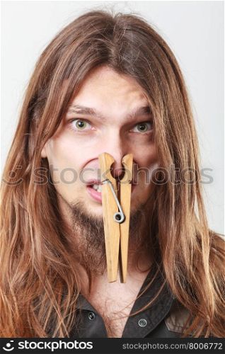 Man with clogged nose by clothespin. Unpleasant bad smell concept. Portrait of young long haired man with clogged nose by big clothespin.