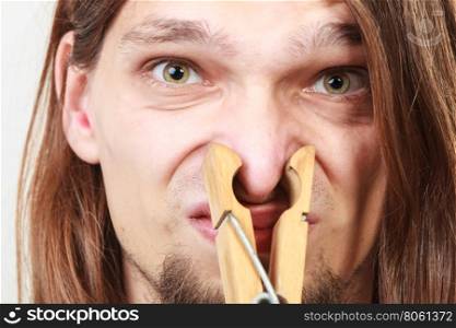 Man with clothespin on nose. Man with clothespin clip peg on his nose. Young long haired guy feeling unpleasant odor stink. Bad smell concept.